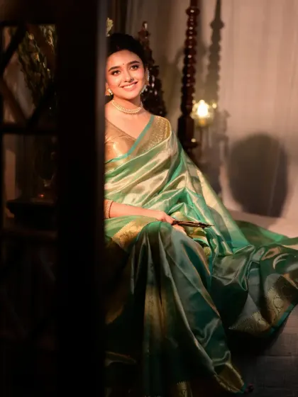 A candid shot of a model in a light green saree, sitting on a traditional swing. The play of shadow and light from the side creates a mysterious and alluring mood.