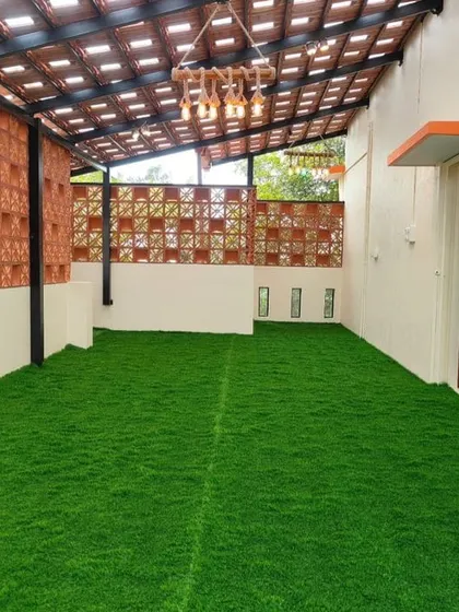 This terrace was transformed into a usable, vibrant space with low-maintenance artificial grass and a decorative terracotta jali wall for privacy. The slatted pergola roof provides partial shade, making it a comfortable extension of the home.