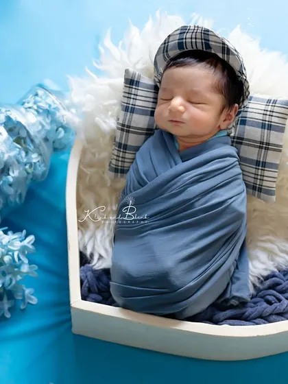 A heart full of love. This baby boy is swaddled in blue and rests in a white heart-shaped bowl, with blue flowers spilling out of a bottle for a pop of color.