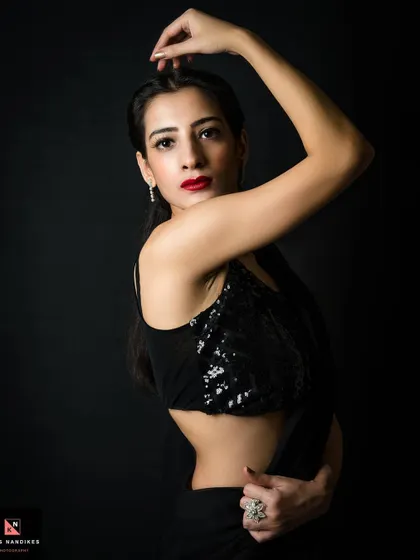A dynamic portrait of a woman in a black sequin saree. Her pose is confident and powerful, and the studio lighting creates beautiful highlights on the sequins and her skin.