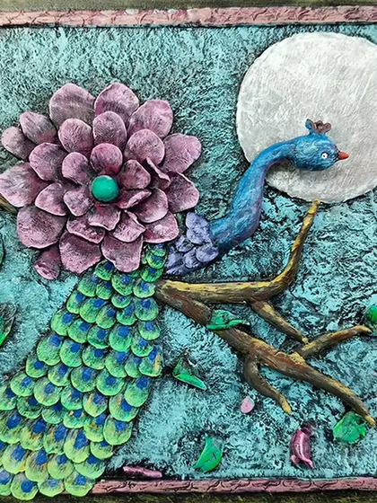 The finished relief artwork: a stunning peacock with textured feathers and a full moon. This piece showcases the beautiful results of our clay and relief work classes.