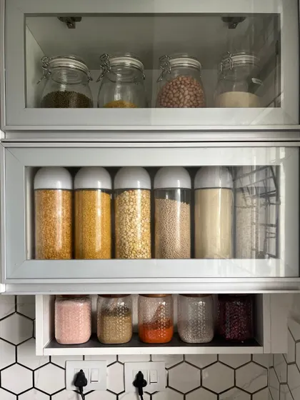 A well organized kitchen cabinet with glass-front doors can be a beautiful feature. Here, we've arranged dals and spices in clear, uniform jars to create a neat and aesthetically pleasing display.