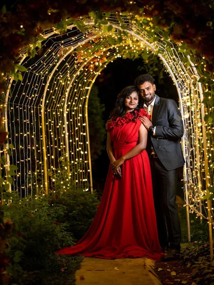 A beautiful night-time shot of a couple standing in a garden path illuminated by an arch of fairy lights, creating a warm and enchanting atmosphere.