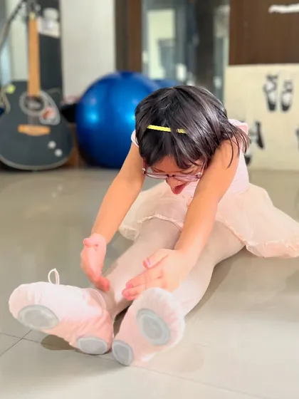 A young student in her pink ballet outfit practices a forward stretch. We focus on making learning fun, even for the youngest dancers.