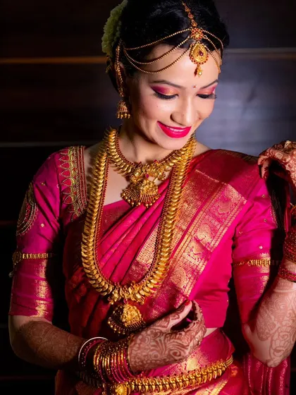 A beautiful bridal portrait, capturing the intricate details of her pink silk saree and gold jewelry.