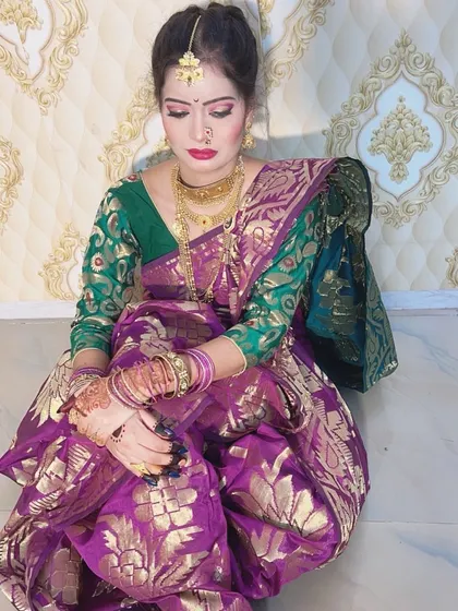 A traditional seated pose of a Maharashtrian bride in a purple and green saree. The makeup is flawless, and the hair is styled in a classic bun, ready for the ceremony.