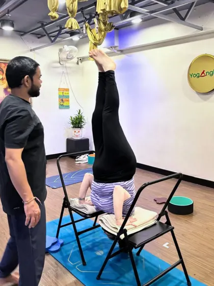 With expert guidance, the impossible becomes possible. Our instructor supervises a student practicing a supported headstand with chairs, ensuring her alignment is correct and she feels secure as she works on this challenging inversion.