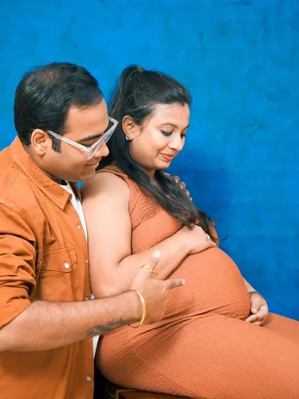 A classic studio maternity portrait. The simple blue backdrop and warm lighting create a timeless and intimate photo of the expectant couple.