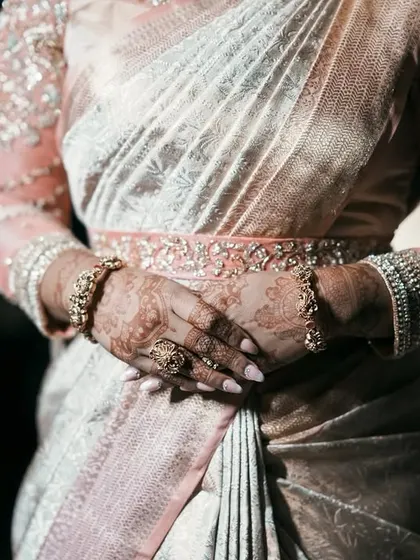 A detail shot focusing on the bride's hands, the embroidered belt, and the heavily worked sheer sleeves of her blouse.