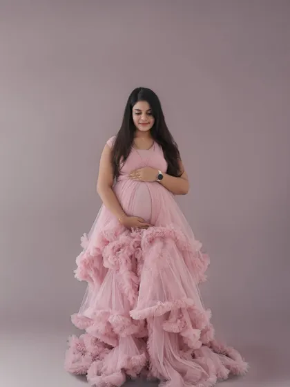 A serene portrait of a mom-to-be in a pink ruffled gown, looking down at her bump. The simple grey background ensures the focus remains on her and the dress.