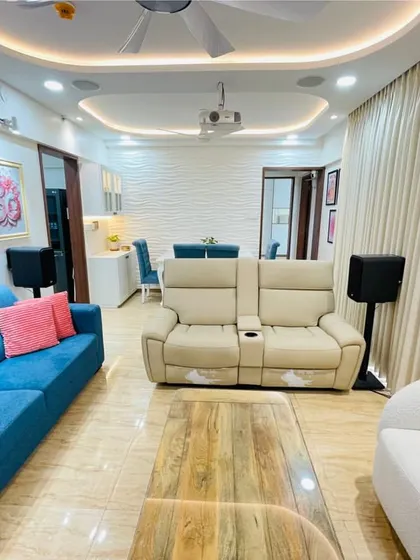 A wider view of the living room with the home theater setup. You can see the rear surround speakers on stands, placed perfectly behind the recliner sofa for an enveloping sound experience.