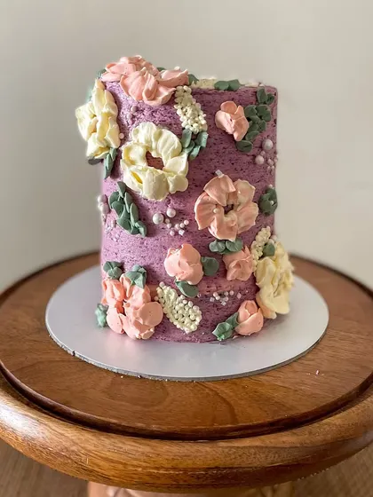 This tall barrel cake is a great example of my floral buttercream work. The textured purple frosting is adorned with hand-piped flowers in pastel pinks and yellows, creating a beautiful garden effect.