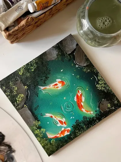 An angled shot of the finished acrylic koi pond painting on my desk. The details of the water ripples and the mossy rocks around the edge are clearly visible.