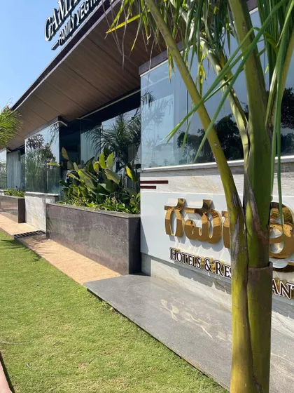 The exterior landscape for Gamashree Restaurant in Sagara. The design uses a clean, manicured lawn and a raised planter bed with tropical plants to create a sharp, modern, and welcoming facade for the hotel and restaurant.
