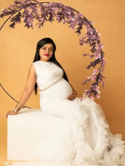 A serene portrait in our white mermaid gown with a ruffled train, seated against a floral hoop for a modern and elegant look.