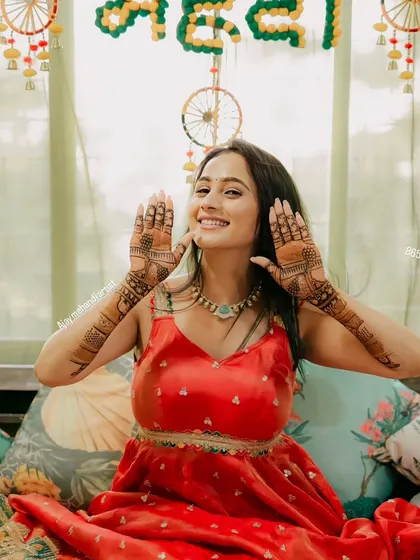 A happy bride showing off her mehndi in front of a festive "Mehndi" backdrop. Her smile says it all.