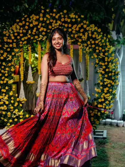 The bride twirls in her colorful lehenga in front of a beautiful yellow floral arch. This photo captures her happiness and the festive atmosphere of the Haldi event.