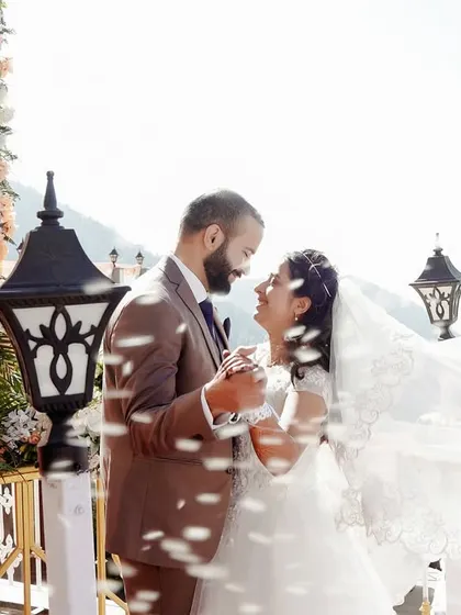 A beautiful, joyful shot of the bride and groom during their outdoor ceremony. The wind catching her veil and the falling petals create a dynamic and magical moment.