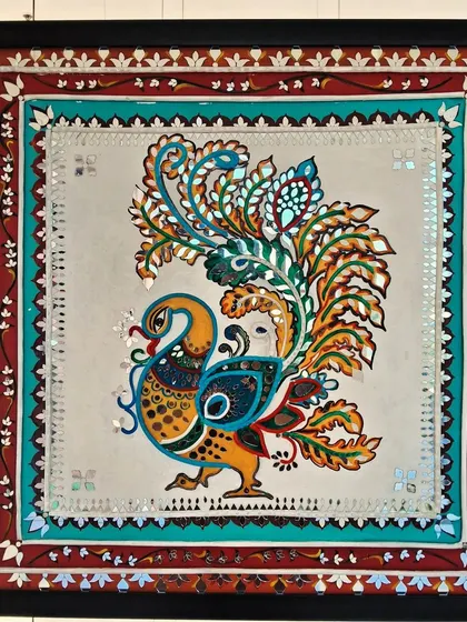 A beautiful mirror-work piece from the 'Aaina' exhibition, depicting a majestic peacock with intricate details and vibrant colors.