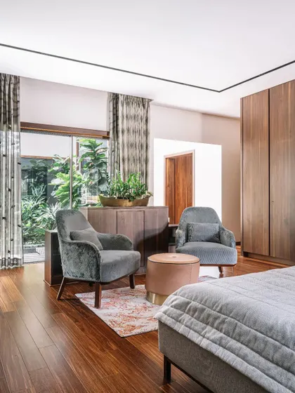 This bedroom is all about clean lines and natural light. The seating area by the window provides a lovely spot to relax and enjoy the garden view. The wooden wardrobe and flooring add a sense of warmth and earthiness to the modern design.