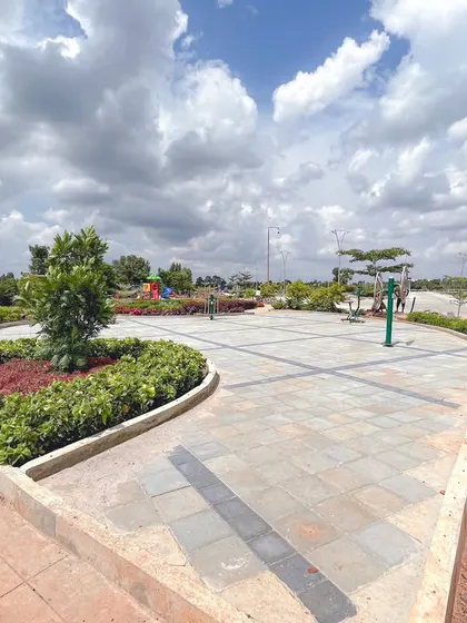 A wide plaza at 'The Sanctuary' with geometric paving, surrounded by colorful planting beds, provides a versatile open space for community use.