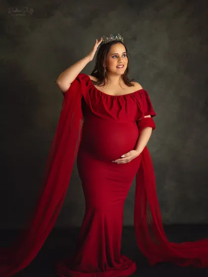 A full-length portrait of a queen awaiting her heir. The crown and the elegant red gown with its sheer train create a truly majestic and memorable maternity photo.