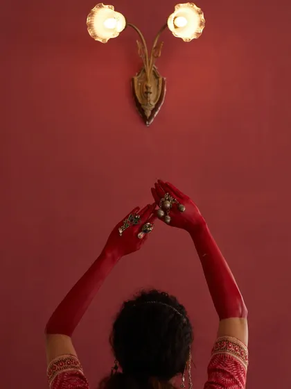 An artistic composition where the model's painted hands are raised towards a vintage wall lamp. This creative shot tells a story, using symbolism and colour to evoke a specific mood for the fashion campaign.