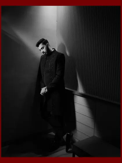 A dramatic black and white portrait of the groom. The strong shadows and focused lighting create a powerful and stylish image, showcasing his sharp attire and confident presence.