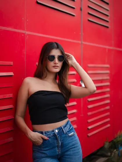 A cool and confident street style portrait. The model's simple outfit against the bright red background creates a bold and modern look.