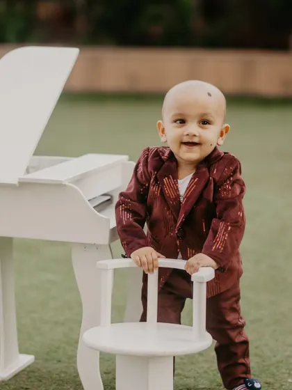 A happy little musician stands by his miniature piano, dressed in a sparkling velvet suit for his birthday photoshoot.