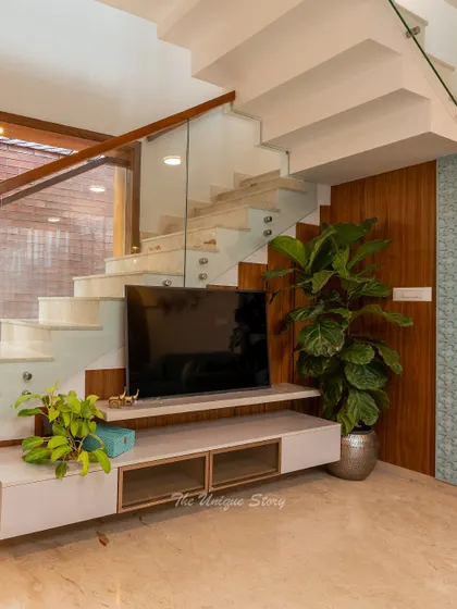 A close-up of the clever under-stair TV unit solution. This custom design maximizes usable space in the living room while maintaining a clean and uncluttered look, framed by a modern glass staircase railing.