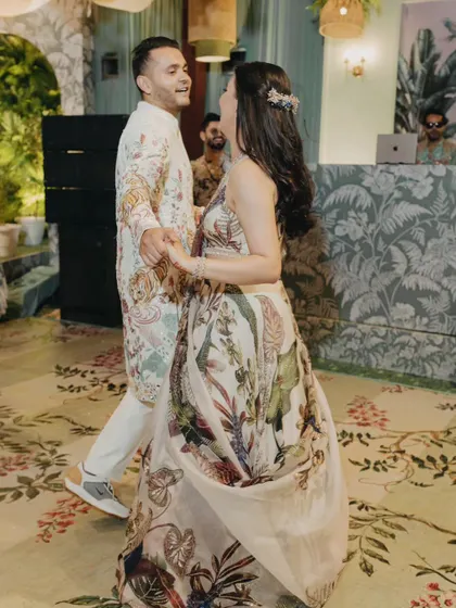 The couple shares their first dance at a tropical-themed welcome soiree. Their coordinated floral outfits perfectly match the lush, nature-inspired decor and custom-printed carpet.
