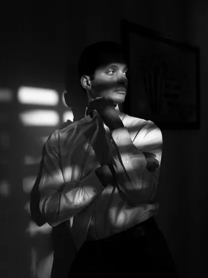 A dramatic black and white portrait of a groom, with shadows from a window creating stripes of light across him. This is a moody, cinematic shot that showcases a fine-art approach.
