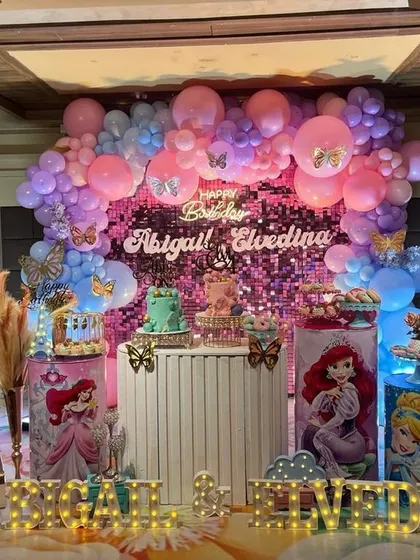 A dreamy Disney Princess party featuring a sparkling pink shimmer wall, character-themed cake plinths, and beautiful balloon arrangements with butterfly details.