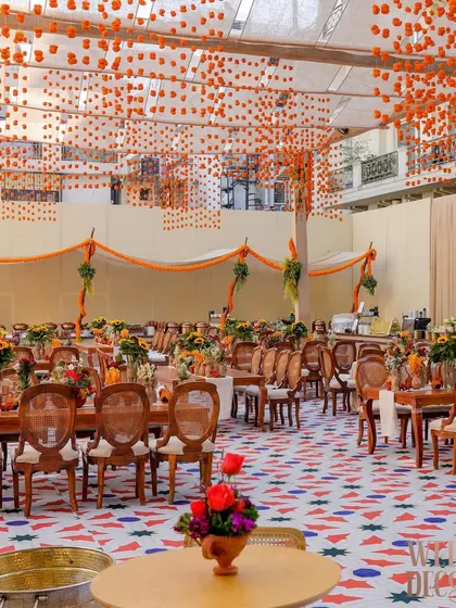 A wide shot of the dining area under a canopy of hanging marigold buds. The custom-printed geometric floor in red, white, and blue adds a contemporary touch to the traditional Indian decor elements.