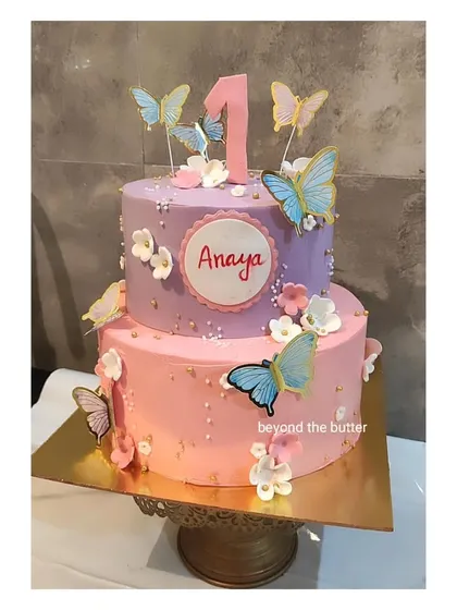 Another example of a butterfly-themed cake, this one for a first birthday. The two tiers in pink and purple are decorated with colorful butterflies and a personalized name plaque.