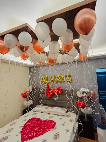 An elegant anniversary decoration with 'Always Love' foil balloons, a heart of rose petals, and a canopy of white and rose gold balloons.