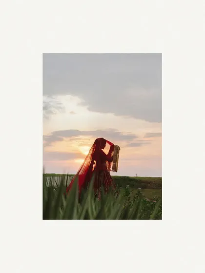 A silhouette of the bride against a sunset sky, her veil flowing in the wind, creating a dramatic and beautiful image.