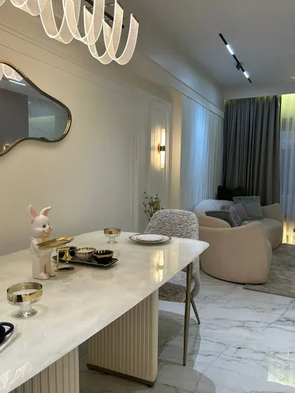 A full view of this elegant dining and living area. The marble-top dining table, modern chandelier, and plush sofa come together to create a space that feels luxurious, bright, and welcoming.