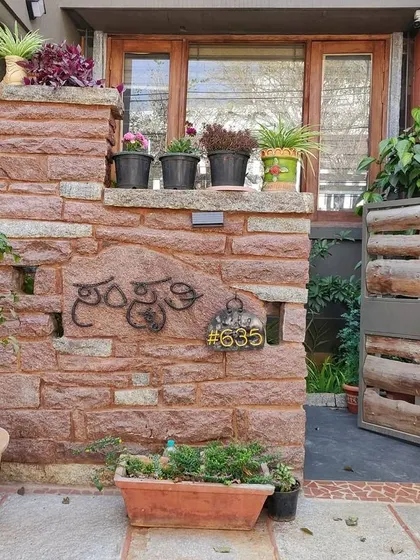 The entrance to this home, named 'Samskruthi', features a natural stone compound wall and a gate made from reclaimed wood logs. These earthy materials create a warm, inviting, and distinctly personal welcome.