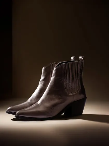 A minimalist shot of dark leather ankle boots. The dramatic, focused lighting highlights the sleek silhouette of the boots, giving them a sophisticated and modern feel.