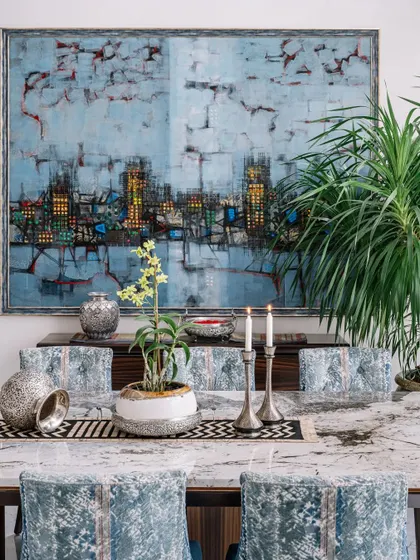 A closer look at the dining table setting, where the texture of the chairs and the pattern of the table runner complement the dramatic cityscape art on the wall. Every detail is chosen to contribute to the overall feeling of refined luxury.