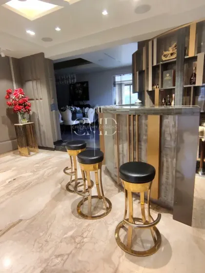 The custom bar in the Gurgaon living space features sleek stools with golden accents and a well-lit back display, making it a perfect spot for hosting.