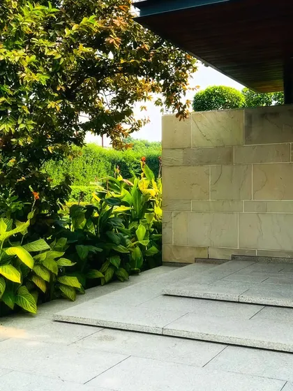A covered patio area provides a shaded transition from the house to the garden. The stone flooring and wall connect seamlessly with the natural elements outside.