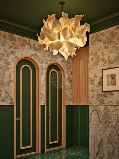Another view of the men's washroom, showcasing the interplay of textures between the Chinoiserie wallpaper, green paneling, and the soft light from the petal-detail chandelier.