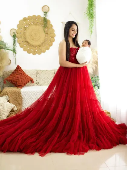 A wide shot showing the magnificent trail of the mother's red gown as she holds her newborn. This adds a touch of glamour and drama to the portrait.