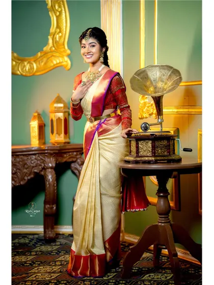 A full-length shot of Amrutha Prem in a classic pose, showcasing the timeless elegance of a silk saree and traditional jewelry.