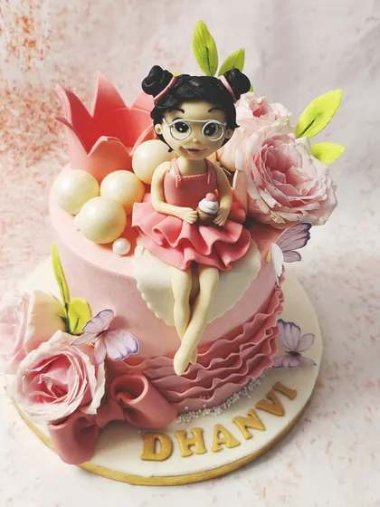 We design a cake fit for a modern princess. A custom-made fondant girl with glasses and a pink dress sits among fresh roses, delicate butterflies, and a pink crown, creating a personalized and enchanting birthday centerpiece.