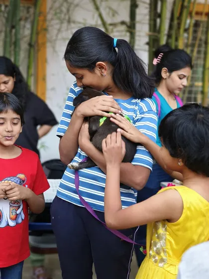 A group of children gather around to cuddle a small black puppy. These moments of shared affection are what our adoption drives are all about.