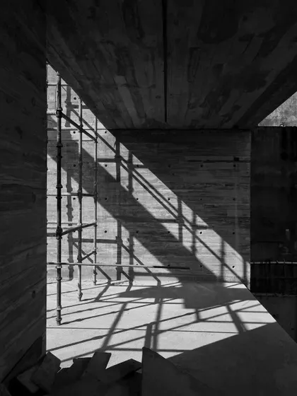 The play of light and shadow on an unfinished concrete wall. The diagonal shadows are cast by the scaffolding, creating a temporary geometric pattern on the surface.